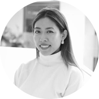 Une femme brune aux traits asiatiques, qui sourit. Elle porte un col roulé blanc
