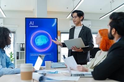 Image of a team working at a table with a smart board in the background